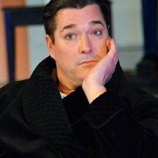 Charles Condomine sitting in black bathrobe with head in hand looking exhausted